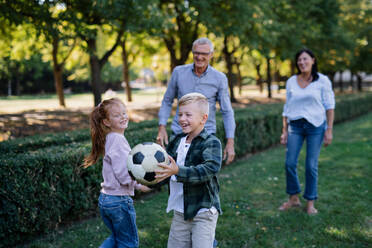 Glückliche kleine Kinder mit Großeltern spielen mit Ball im Freien in einem Park - HPIF08338