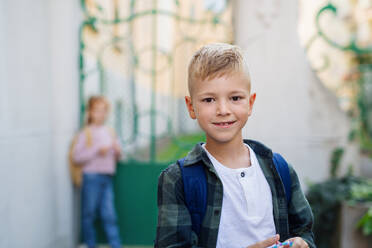 Ein glücklicher kleiner Schuljunge schaut vor der Schule in die Kamera. - HPIF08343