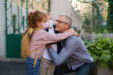 Ein glücklicher Großvater, der seine Enkelkinder von der Schule nach Hause bringt und vor der Schule auf der Straße wartet. - HPIF08344