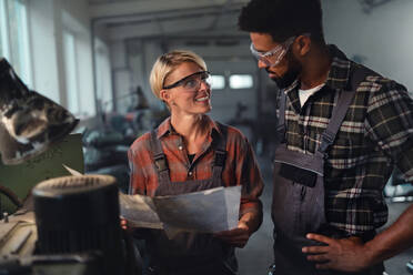 Ein Porträt von jungen, gemischtrassigen Arbeitskollegen, die in einer Metallwerkstatt arbeiten, lächelnd - HPIF08352