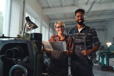 Ein Porträt von jungen, gemischtrassigen Arbeitskollegen, die in einer Metallwerkstatt arbeiten, lächeln und in die Kamera schauen. - HPIF08353