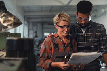 Ein Porträt von jungen, gemischtrassigen Arbeitskollegen, die in einer Metallwerkstatt arbeiten, lächelnd - HPIF08356