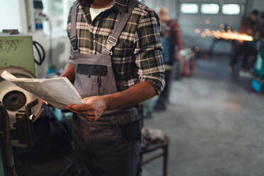 Nahaufnahme eines jungen Industriearbeiters, der in einer Metallwerkstatt Blaupausen in der Hand hält. - HPIF08360