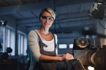 Ein Porträt einer erwachsenen Frau, die in einer Metallwerkstatt arbeitet und in die Kamera schaut. - HPIF08367