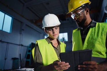 Niedriger Blickwinkel auf Industrieinspektoren mit Tablet, die in einer Metallwerkstatt eine allgemeine Kontrolle durchführen und sich unterhalten. - HPIF08387