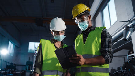 Niedriger Blickwinkel auf Industrieinspektoren mit Gesichtsmasken, die in einer Metallwerkstatt eine allgemeine Kontrolle durchführen, Konzept des Coronavirus. - HPIF08389