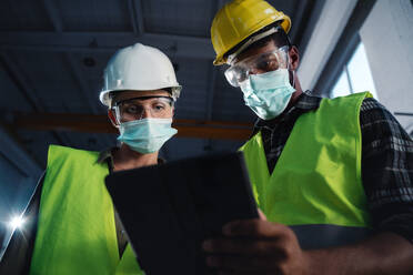 Niedriger Blickwinkel auf Industrieinspektoren mit Gesichtsmasken, die in einer Metallwerkstatt eine allgemeine Kontrolle durchführen, Konzept des Coronavirus. - HPIF08390