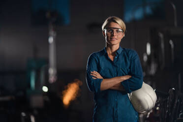 A portrait of mid adult industrial woman working indoors in metal workshop, looking at camera. - HPIF08395