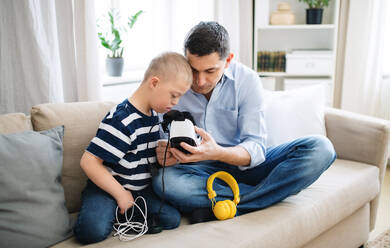 Ein Vater mit einem glücklichen Sohn mit Down-Syndrom zu Hause, der eine VR-Brille benutzt. - HPIF08405