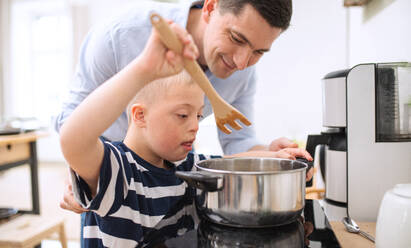 Ein Vater mit einem glücklichen Sohn mit Down-Syndrom in der Küche beim Kochen. - HPIF08411