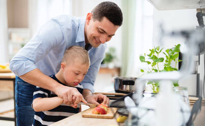 Ein Vater mit einem glücklichen Sohn mit Down-Syndrom in der Küche, der einen Apfel hackt. - HPIF08413