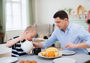 Eine glückliche Familie mit einem Sohn mit Down-Syndrom sitzt am Tisch und frühstückt. - HPIF08414