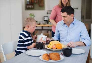 Eine glückliche Familie mit einem Sohn mit Down-Syndrom sitzt am Tisch und frühstückt. - HPIF08415