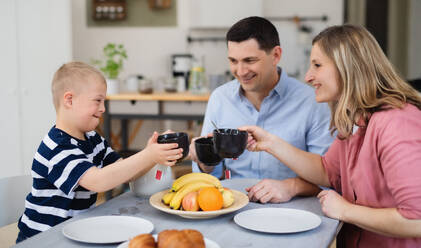 Eine glückliche Familie mit einem Sohn mit Down-Syndrom sitzt am Tisch und frühstückt. - HPIF08416
