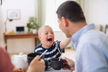 Eine glückliche Familie mit einem Sohn mit Down-Syndrom, der lachend am Tisch frühstückt. - HPIF08421