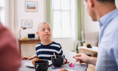 Ein Porträt eines Jungen mit Down-Syndrom, der mit seinen Eltern am Tisch frühstückt. - HPIF08428