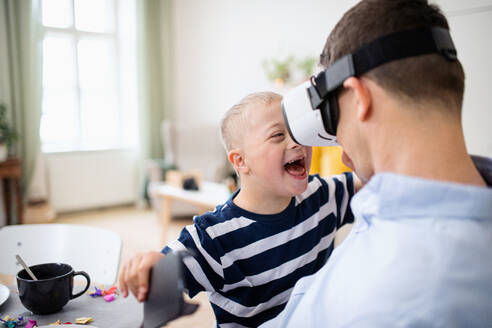 Ein Vater mit einem glücklichen Sohn mit Down-Syndrom zu Hause, der eine VR-Brille benutzt. - HPIF08429