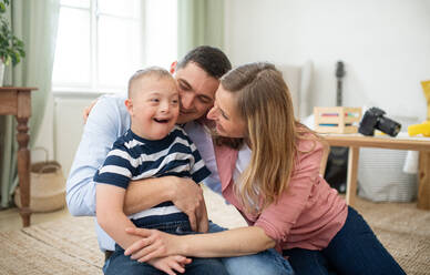 Ein fröhlicher Junge mit Down-Syndrom, dessen Eltern zu Hause sind und sich umarmen und lachen. - HPIF08432