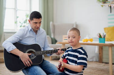 Ein fröhlicher Junge mit Down-Syndrom und Vater, der lachend Musikinstrumente spielt. - HPIF08434