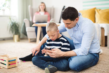 A father with happy down syndrome son indoors at home, using smartphone. - HPIF08439