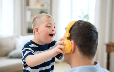 Ein glücklicher Junge mit Down-Syndrom und Vater zu Hause, der sich mit Kopfhörern amüsiert. - HPIF08440