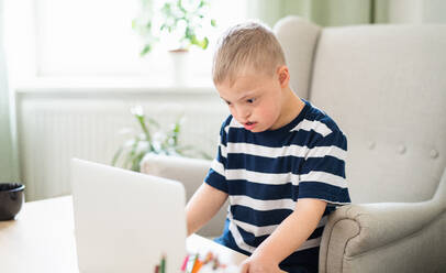 Ein Junge mit Down-Syndrom, der zu Hause einen Laptop benutzt. - HPIF08446