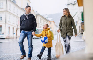 Eine glückliche Familie mit einem Sohn mit Down-Syndrom geht im Freien spazieren und trägt Einkäufe. - HPIF08452