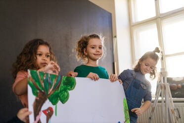 Eine Gruppe glücklicher kleiner Mädchen hält ein Bild in der Hand, das sie im Kunst- und Bastelunterricht in der Schule gemalt haben - HPIF08482