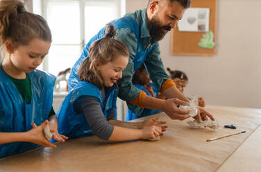Eine Gruppe kleiner Kinder mit einem Lehrer, die während des Kunst- und Bastelunterrichts in der Schule mit Ton arbeiten. - HPIF08490