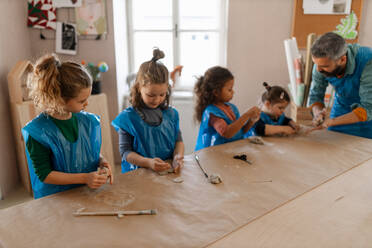 A group of little kids with teacher working with pottery clay during creative art and craft class at school. - HPIF08492