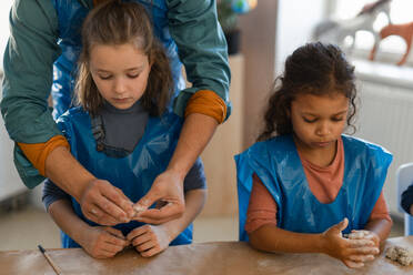 Little kids with a teacher working with pottery clay during creative art and craft class at school. - HPIF08494