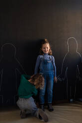 Rückansicht eines kleinen Mädchens, das seine Freunde mit Kreide auf einer Wandtafel im Spielzimmer zeichnet. - HPIF08508