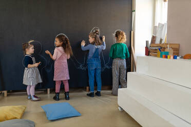 A group of little girls posing in front of blackboard wall paintings indoors in playroom. - HPIF08509