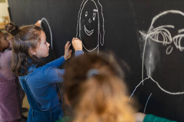 Kleine Mädchen zeichnen mit Kreiden auf einer Tafel Wand drinnen im Spielzimmer. - HPIF08510