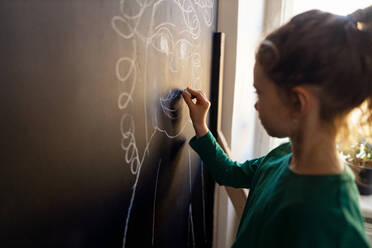 Ein kleines Mädchen Zeichnung mit Kreiden auf Tafel Wand drinnen im Spielzimmer. - HPIF08513