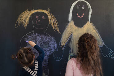Eine Rückansicht einer Gruppe kleiner Mädchen, die mit Kreiden auf einer Tafel im Spielzimmer zeichnen. - HPIF08514