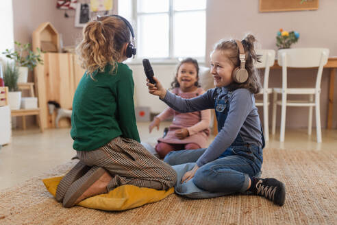 Glückliche kleine Mädchen mit Kopfhörern und Mikrofon, die ein Interview führen, Spaß haben und zu Hause spielen. - HPIF08531