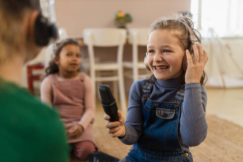 Glückliche kleine Mädchen mit Kopfhörern und Mikrofon, die ein Interview führen, Spaß haben und zu Hause spielen. - HPIF08532