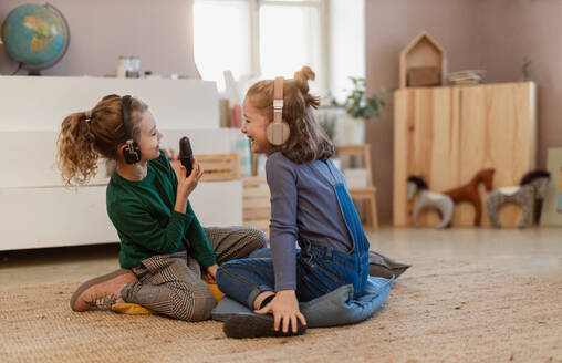 Glückliche kleine Mädchen mit Kopfhörern und Mikrofon, die ein Interview führen, Spaß haben und zu Hause spielen. - HPIF08533