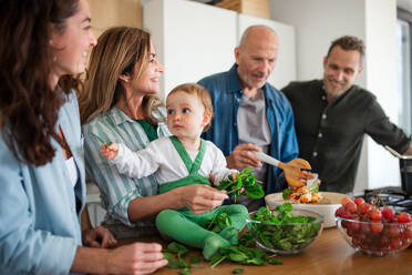 Glückliche Mehrgenerationenfamilie zu Hause, die in der Küche einen Gemüsesalat zubereitet. - HPIF08536