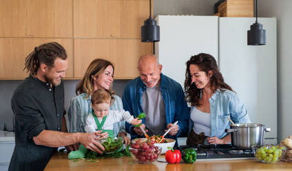 Glückliche Mehrgenerationenfamilie zu Hause, die in der Küche einen Gemüsesalat zubereitet. - HPIF08537