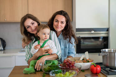 Porträt einer reifen Mutter mit Tochter und Enkelin in einem Haus, die beim Kochen in die Kamera schauen. - HPIF08540