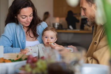 Porträt eines glücklichen Paares, das zu Hause am Tisch zu Mittag isst und sein Baby füttert. - HPIF08550