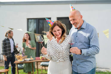 Ein reifes Paar mit Wein im Freien im Garten zu Hause, Geburtstagsfeier Party. - HPIF08580
