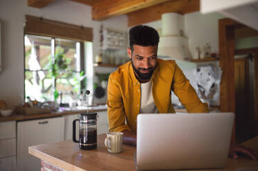 Ein junger Mann mit Laptop und Kaffee arbeiten drinnen, Home-Office-Konzept. - HPIF08600