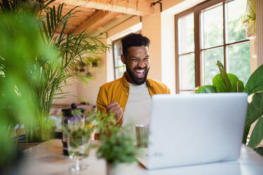 Ein fröhlicher junger Mann mit Laptop arbeitet drinnen, Home-Office-Konzept. - HPIF08606