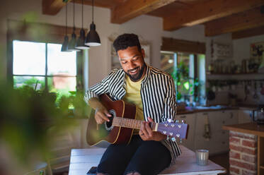 Porträt eines glücklichen jungen Mannes mit Gitarre, der sich zu Hause entspannt. - HPIF08609