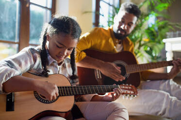Ein glücklicher Vater mit einer kleinen Tochter, die zu Hause Gitarre spielt. - HPIF08652