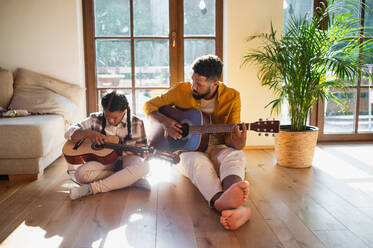 Frontansicht eines glücklichen Vaters mit seiner kleinen Tochter, die zu Hause Gitarre spielt. - HPIF08653