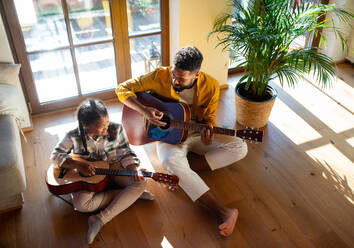 A high-angle view of happy father with small daughter indoors at home, playing guitar. - HPIF08654